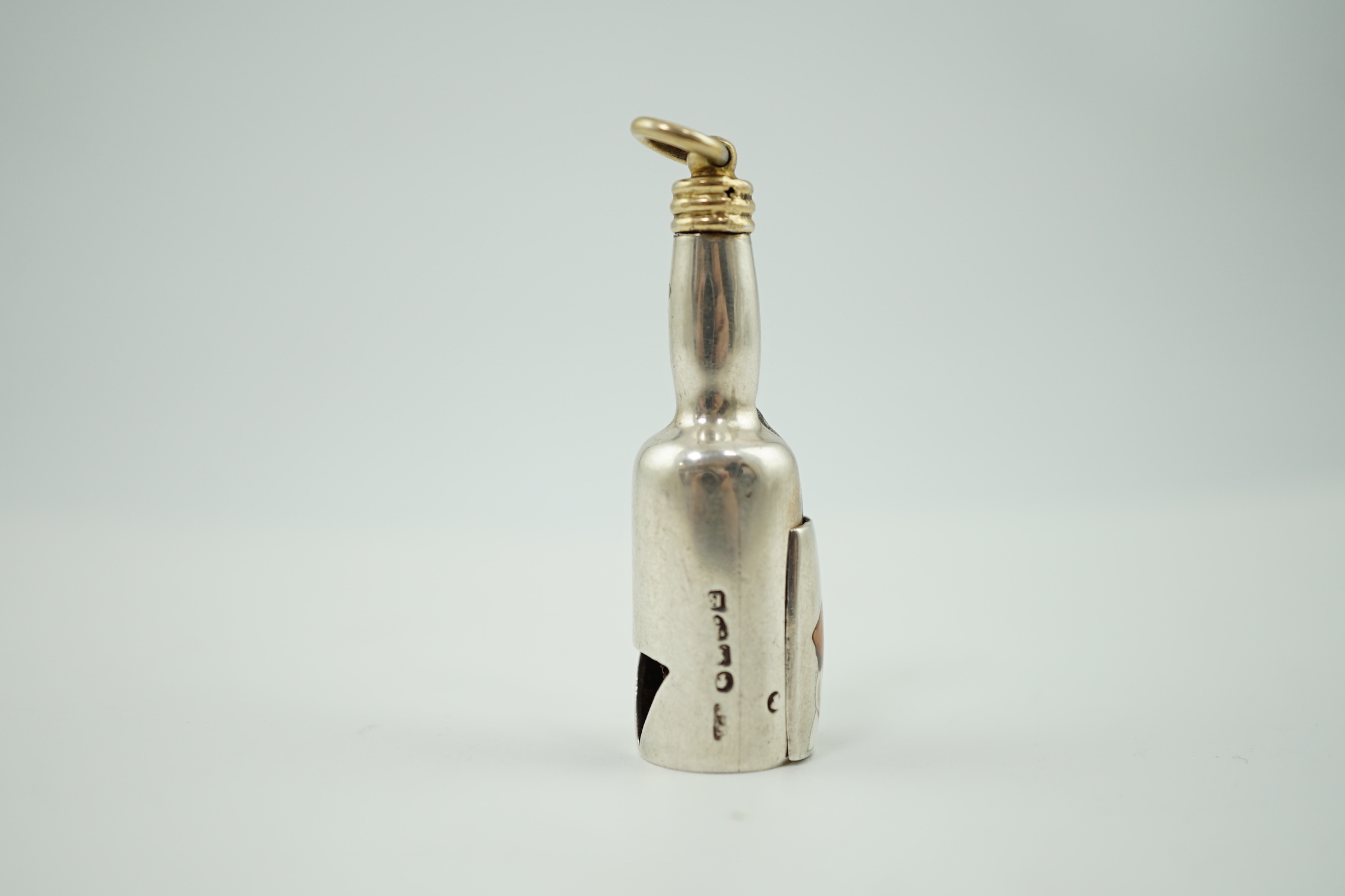 A late Victorian novelty parcel gilt silver cigar cutter, modelled as a bottle, the hinged section enamelled with a head of a dog